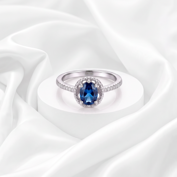 Anillo de compromiso halo con circonia azul zafiro ovalada y pavé de circonias blancas para mujer marca Belle en plata 925 rodinada.