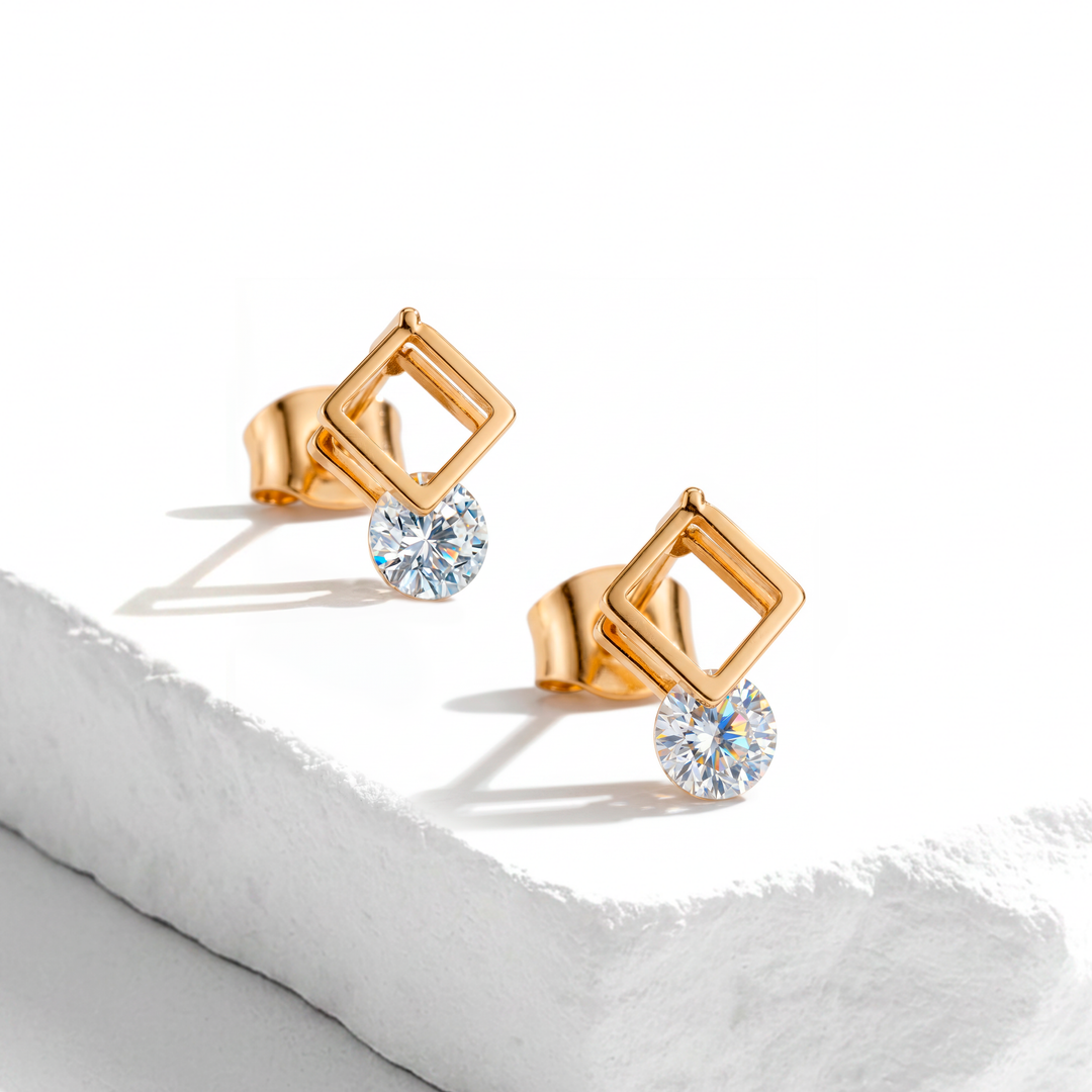 Aretes de botón para muje en acero inoxidable dorado, con diseño de marco cuadrado calado y un cristal redondo blanco facetado colgante.