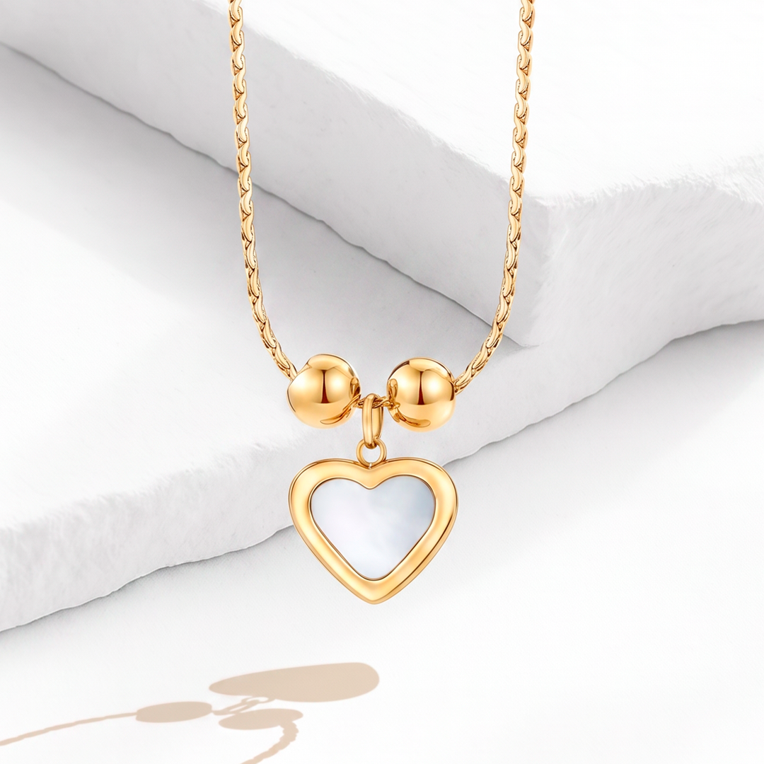 Collar de mujer con cadena trenzada de acero quirúrgico 316 con baño de oro de 18k, que incluye un dije colgante de corazón de nácar blanco enmarcado por dos esferas doradas.