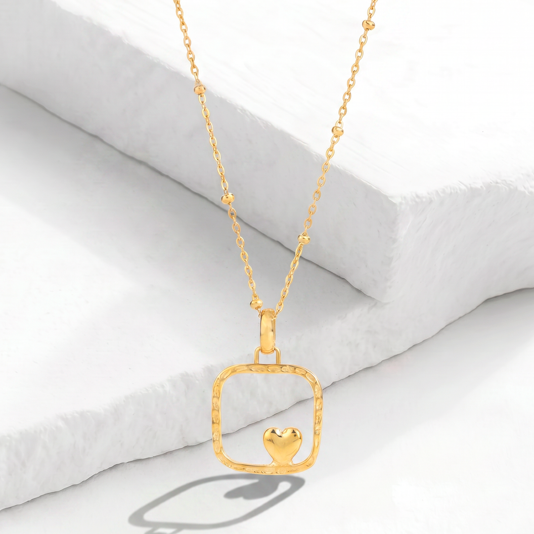 Collar para mujer marca Belle con cadena fina de acero inoxidable bañado en oro de 18k y dije de placa cuadrada dorada mate con un mini corazón abombado pulido en el centro.