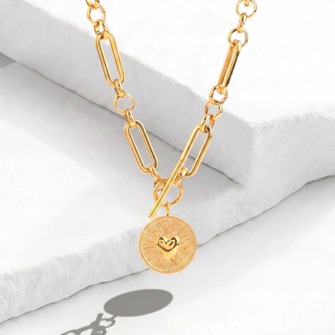 Collar de eslabones alargados para mujer marca Bodo en acero inoxidable bañado en oro de 18k con broche en T y dije de medalla circular labrada con corazón en relieve.