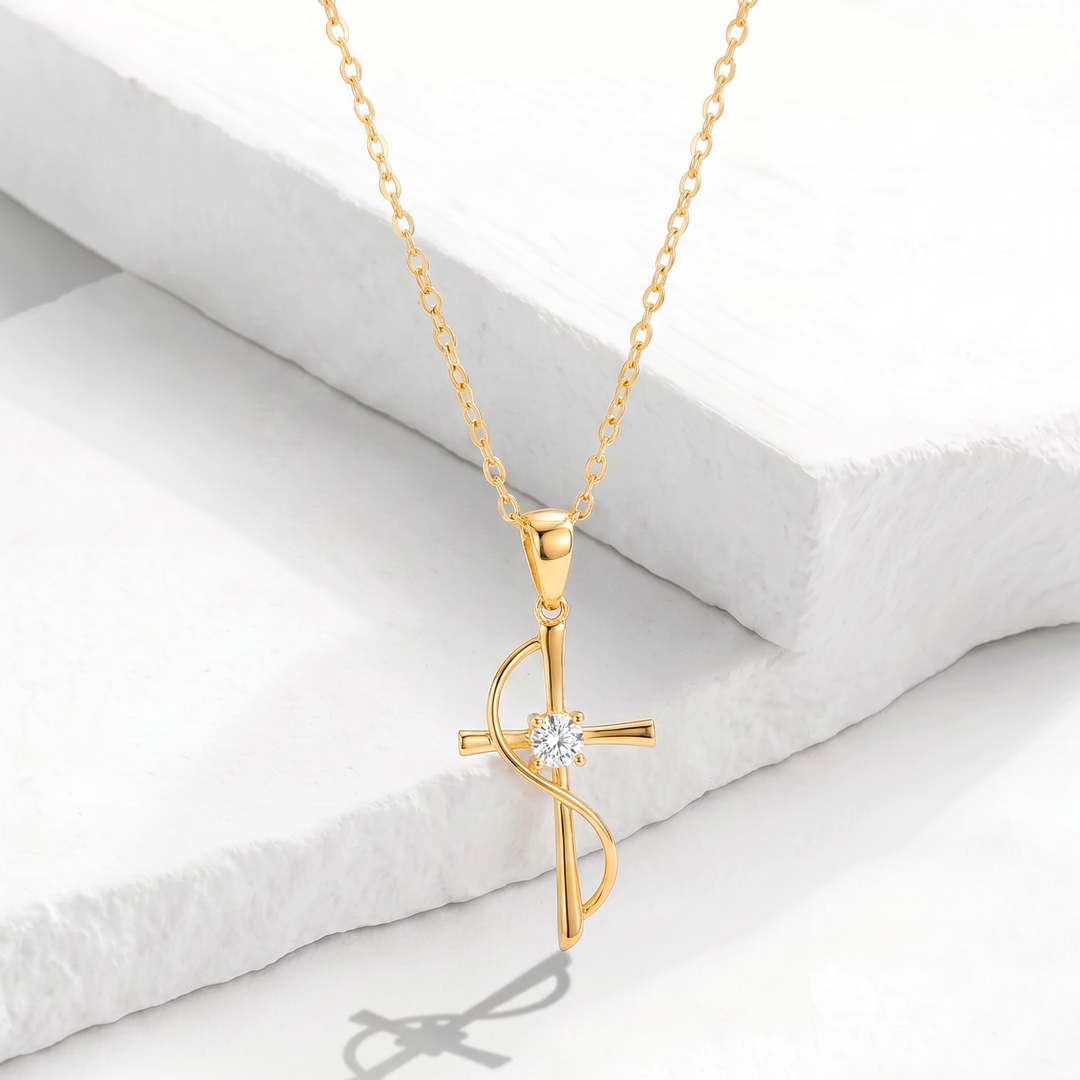 Collar para mujer con cadena fina de acero inoxidable bañado en oro de 18k y dije de cruz de diseño ondeado con un cristal blanco en el centro.