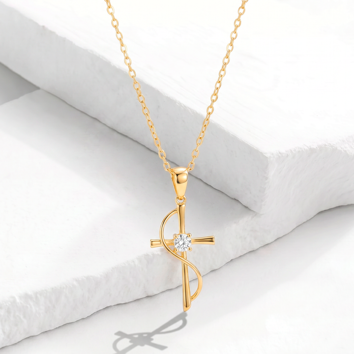 Collar para mujer con cadena fina de acero inoxidable bañado en oro de 18k y dije de cruz de diseño ondeado con un cristal blanco en el centro.