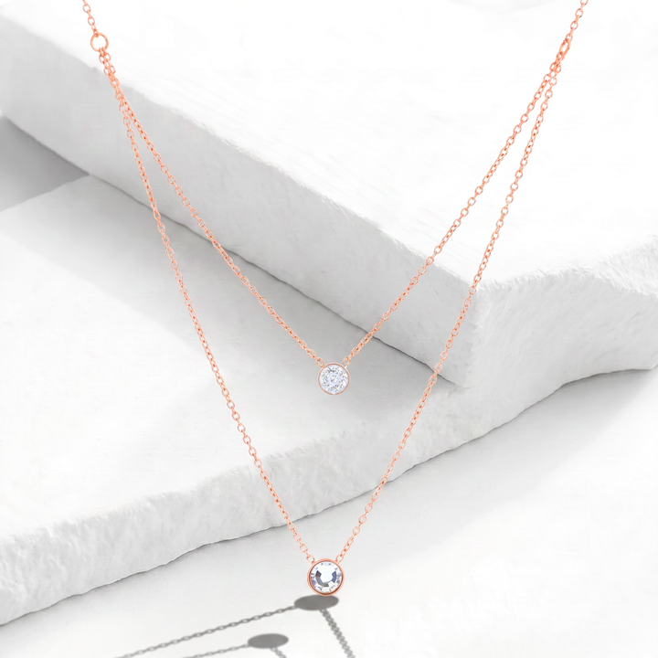 Collar de doble capa para mujer marca Bodo en acero inoxidable bañado en oro rosa con dos dijes circulares punto de luz de cristales blancos.
