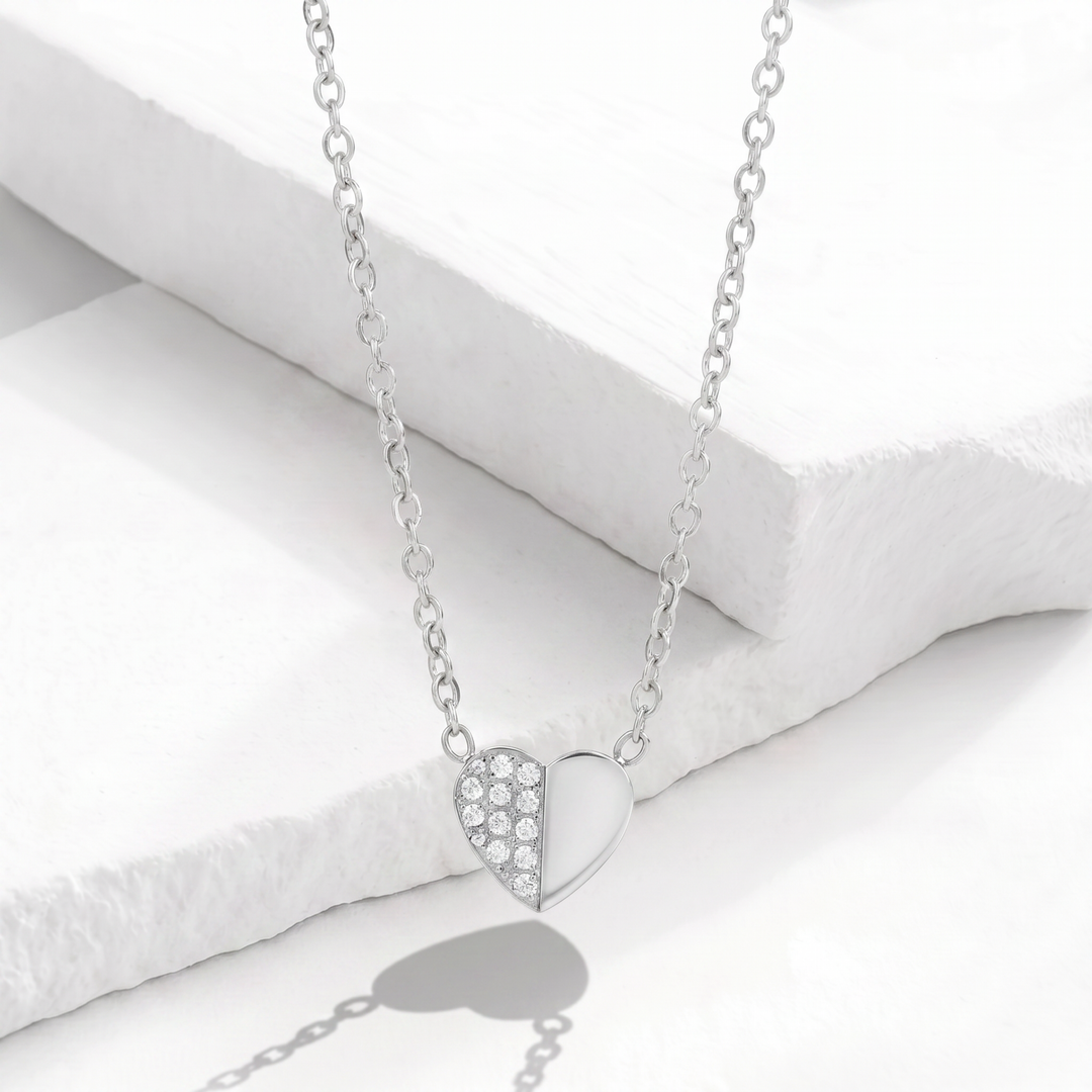 Collar para mujer con cadena fina de acero inoxidable plateado y dije de corazón asimétrico mitad liso pulido y mitad con cristales blancos.