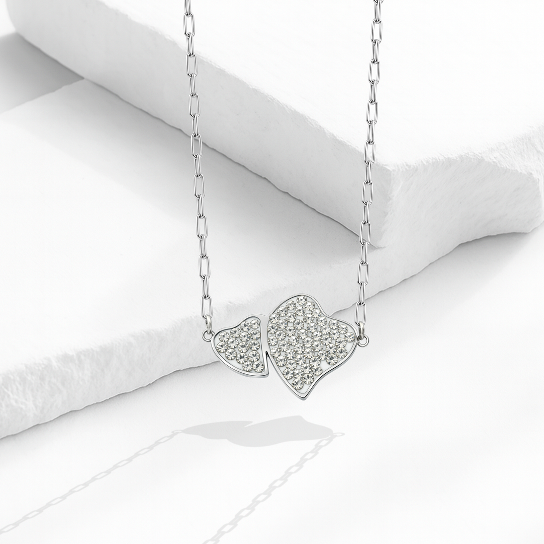 Collar para mujer con cadena de eslabones alargados de acero inoxidable plateado y dije fijo de dos corazones entrelazados cubiertos de cristales blancos en pavé.
