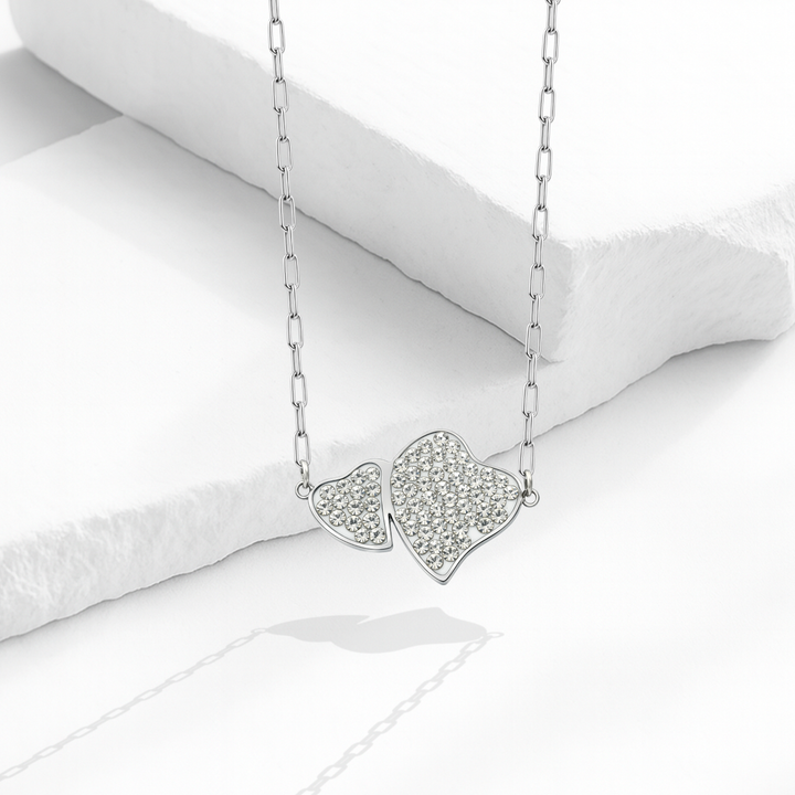 Collar para mujer con cadena de eslabones alargados de acero inoxidable plateado y dije fijo de dos corazones entrelazados cubiertos de cristales blancos en pavé.