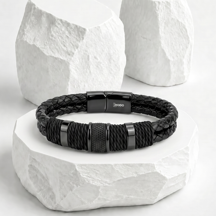 Pulsera para hombre de biocuero negro con costuras blancas, detallada con cordones trenzados, pasador central plateado texturizado y broche magnético de acero inoxidable.