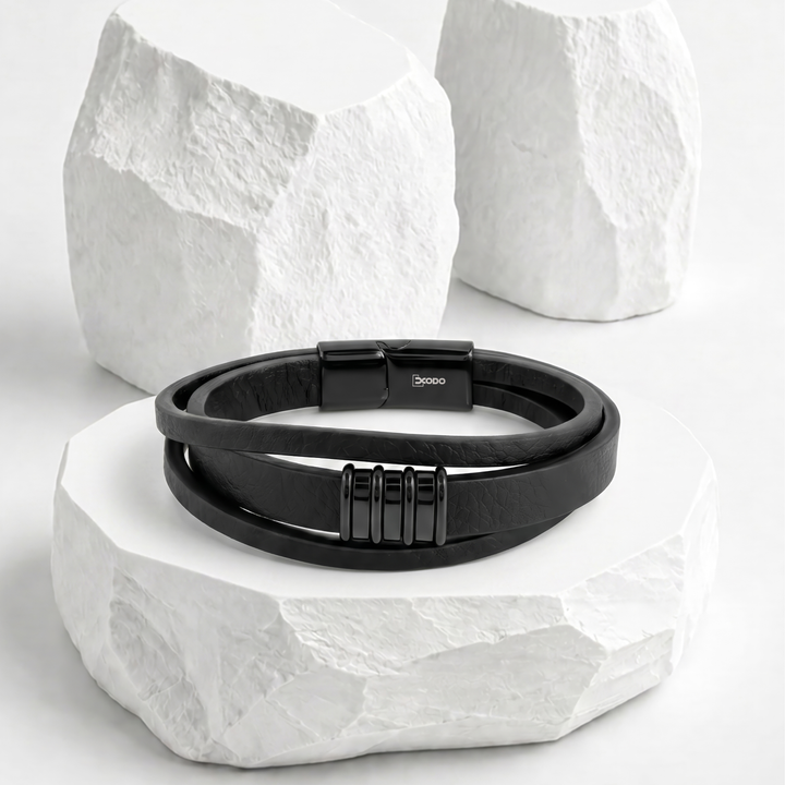 Pulsera para hombre de biocuero negro con diseño de triple banda asimétrica, decorada con un dije de cuatro anillos rectangulares y broche magnético de acero inoxidable negro.