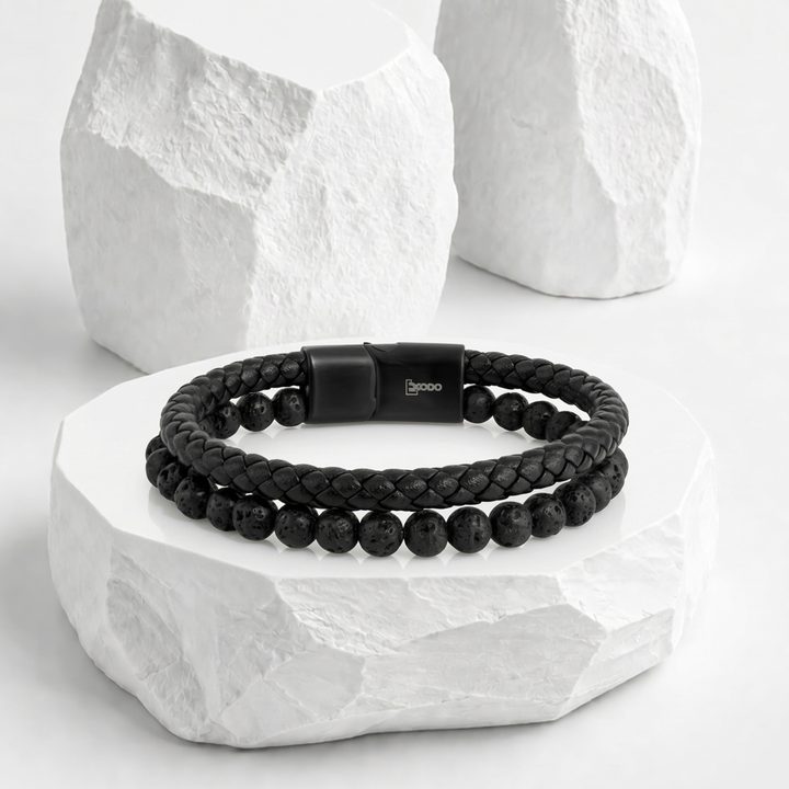 Pulsera negra para hombre marca Éxodo, con diseño de triple capa de biocuero trenzado y una hilera central de esferas de piedra volcánica con broche magnético de acero.