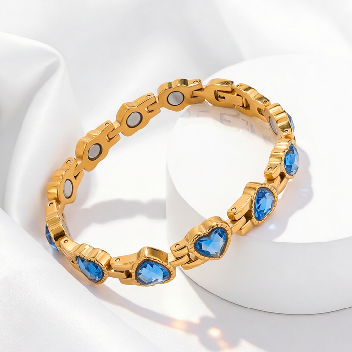 Pulsera magnética para mujer de acero quirúrgico 316 con baño de oro de 18k, formada por eslabones de corazón de cristal azul zafiro e imanes circulares en su cara interna.