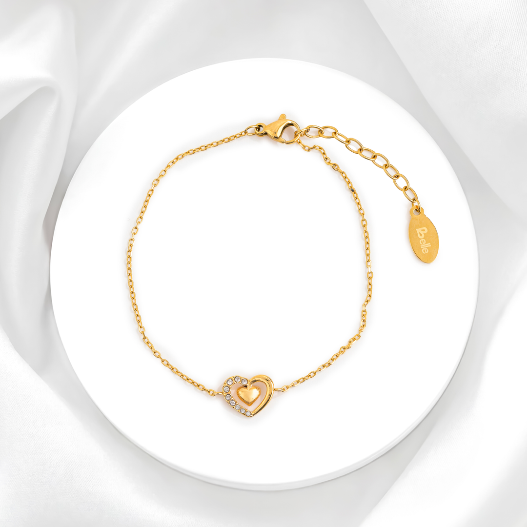Pulsera dorada fina de mujer en acero 316L baño oro 18k con dije de corazón y cristales blancos sobre fondo blanco.