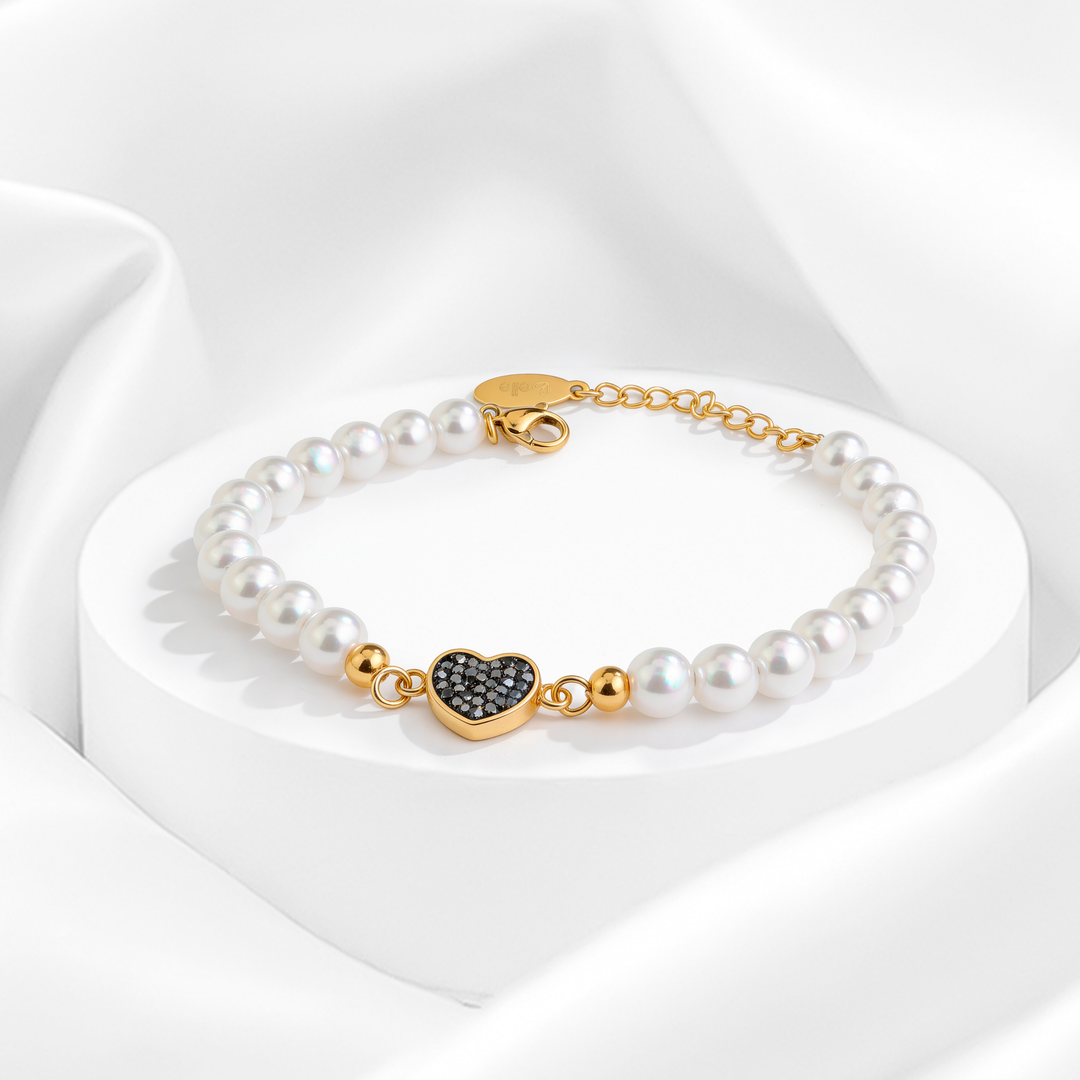Pulsera de perlas blancas para mujer con dije de corazón en cristales negros y cadena dorada de acero 316L bañado en oro 18k.