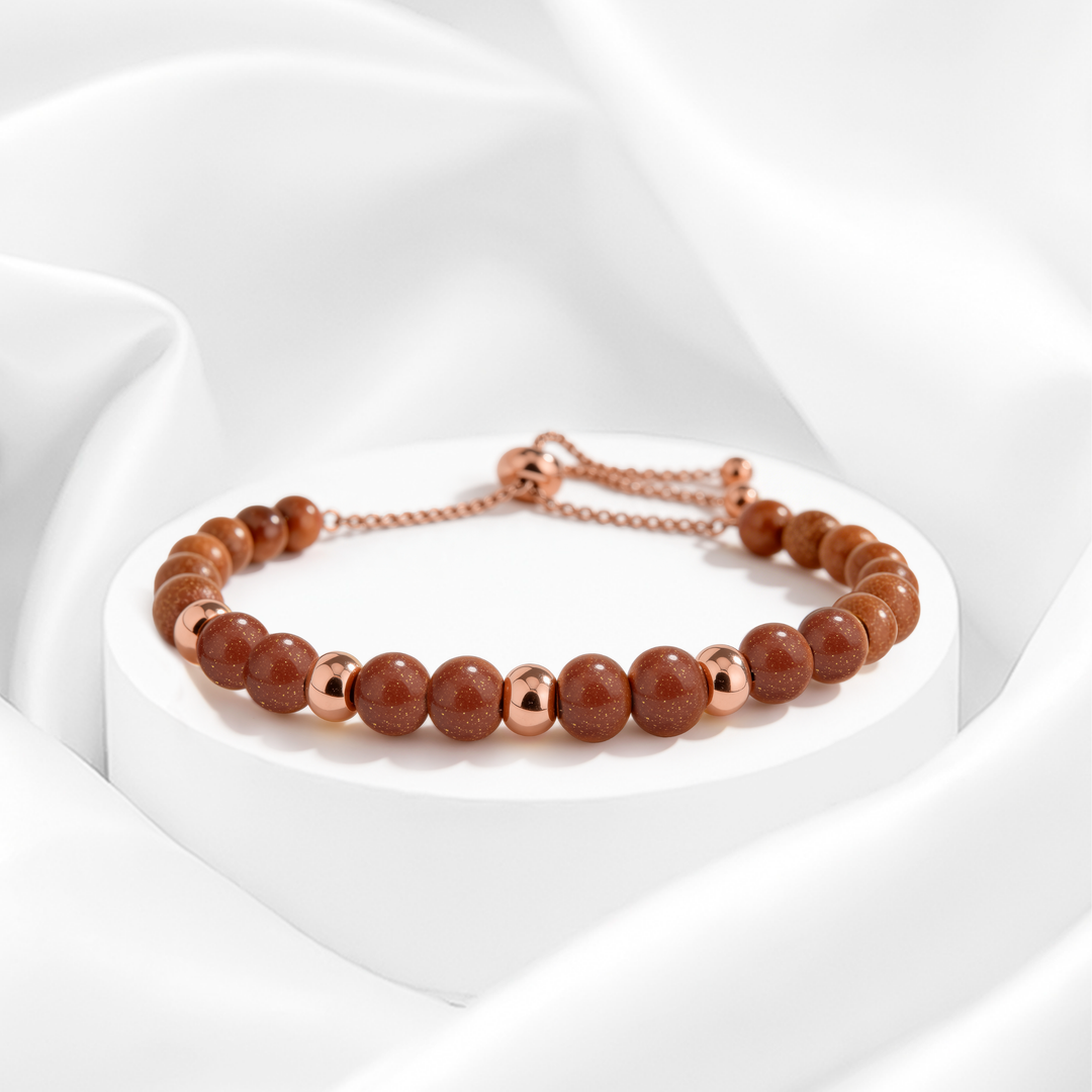 Pulsera dorada de mujer en acero 316L con baño de oro 18k, ajustable con cuentas de piedra rojiza brillante y esferas doradas pulidas.