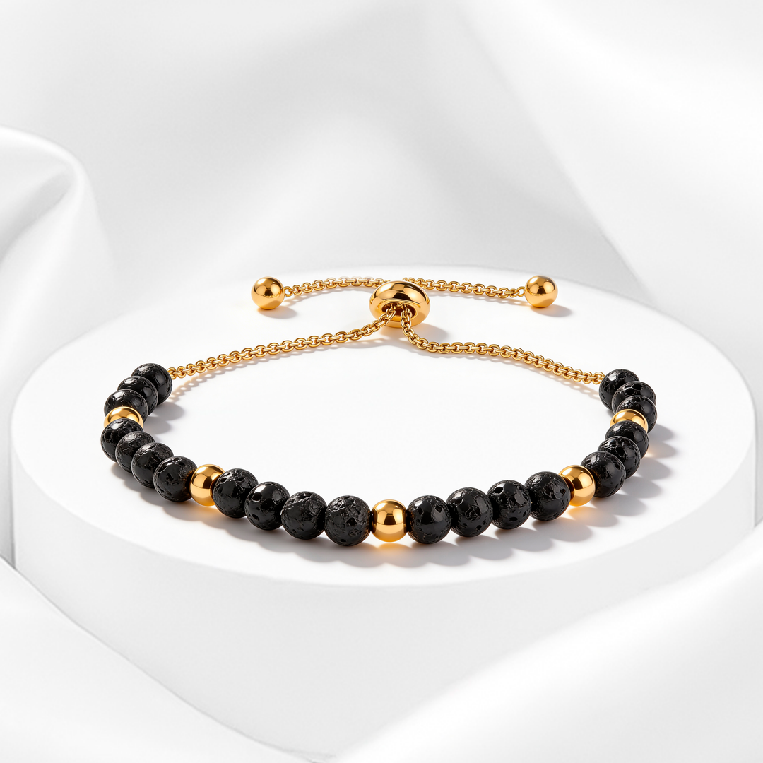 Pulsera dorada de mujer en acero 316L bañado en oro 18k con cuentas de piedra volcánica negra y esferas doradas pulidas sobre fondo blanco.