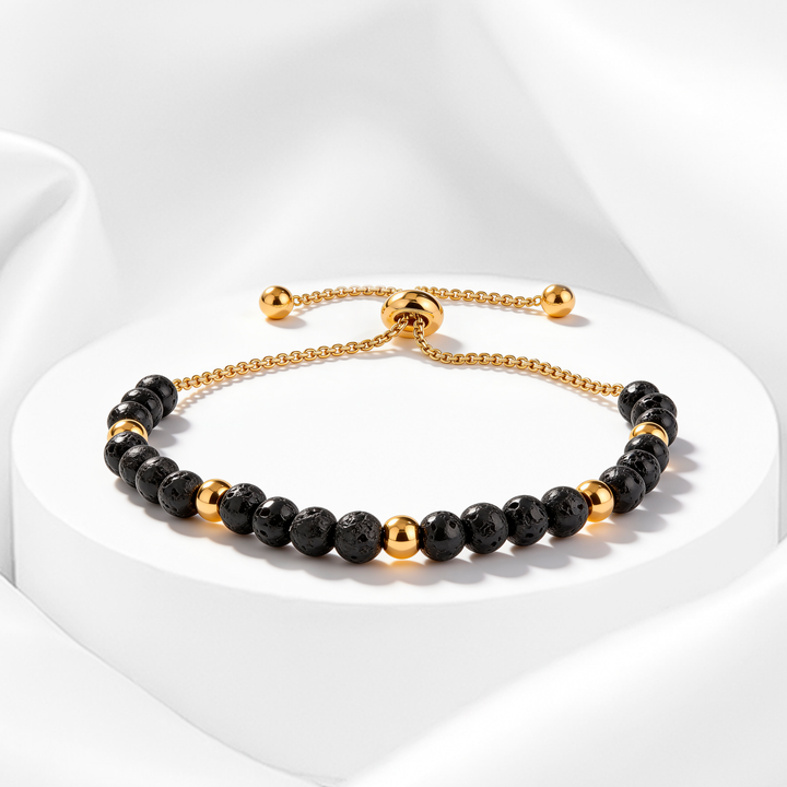 Pulsera dorada de mujer en acero 316L bañado en oro 18k con cuentas de piedra volcánica negra y esferas doradas pulidas sobre fondo blanco.