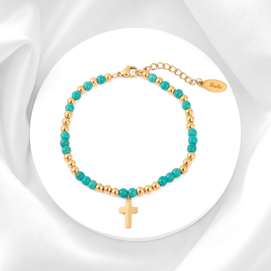 Pulsera para mujer marca Belle confeccionada con cuentas de piedra turquesa e intercalada con esferas de acero bañado en oro de 18k y un dije colgante de cruz dorada pulida.