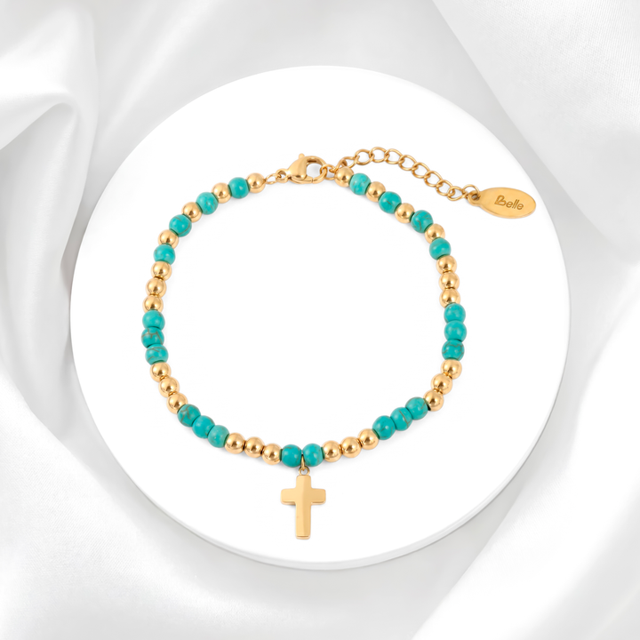 Pulsera para mujer marca Belle confeccionada con cuentas de piedra turquesa e intercalada con esferas de acero bañado en oro de 18k y un dije colgante de cruz dorada pulida.