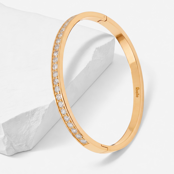 Brazalete rígido de mujer con baño de oro de 18 quilates en acero quirúrgico 316, con una hilera frontal de cristales blancos brillantes engastados y silueta ovalada.