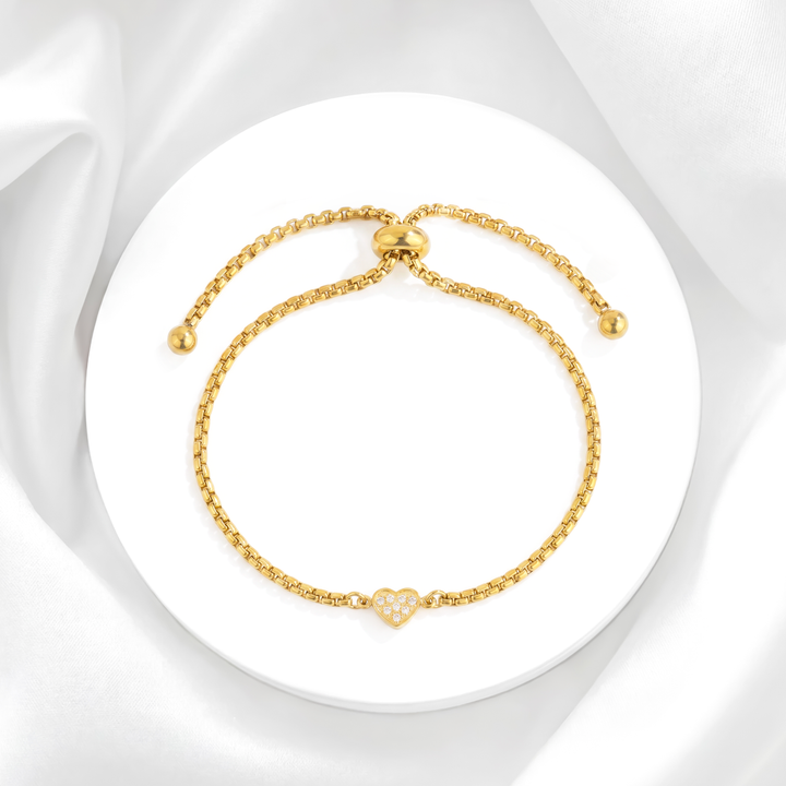 Pulsera ajustable para mujer de acero quirúrgico 316 con baño de oro de 18k, que presenta una cadena fina con cierre slider y un dije de corazón central con cristales blancos.