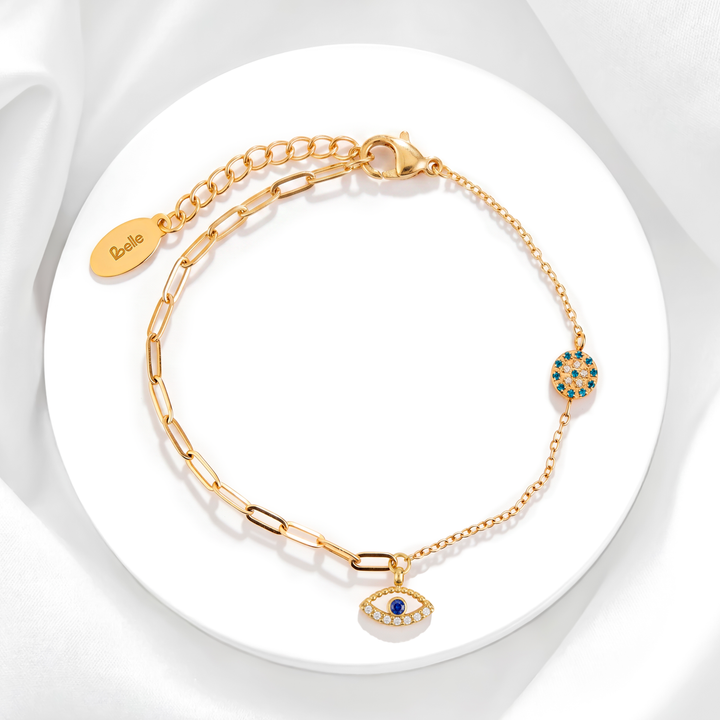 Pulsera mística de mujer en acero quirúrgico 316L baño oro 18k con cadena híbrida de eslabones y dijes de ojo turco con cristales azules y blancos sobre soporte circular.