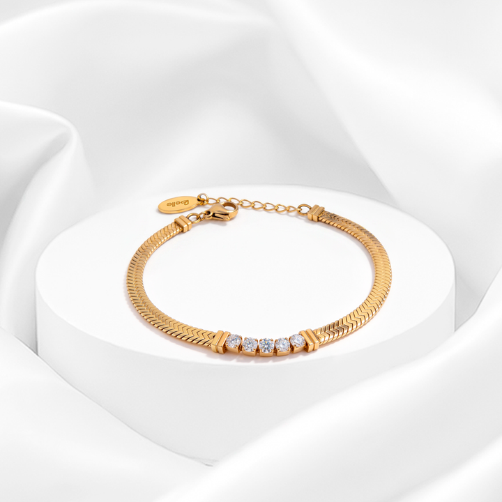 Pulsera dorada de mujer en acero quirúrgico 316 con baño en oro de 18 quilates, diseño de cadena snake plana y cristales blancos centrales sobre soporte circular blanco.
