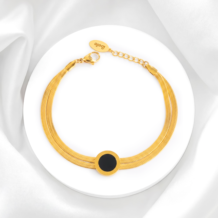 Pulsera dorada para mujer marca Belle de acero quirúrgico 316 con baño de oro de 18k, compuesta por una doble cadena plana estilo snake y un dije circular central negro.