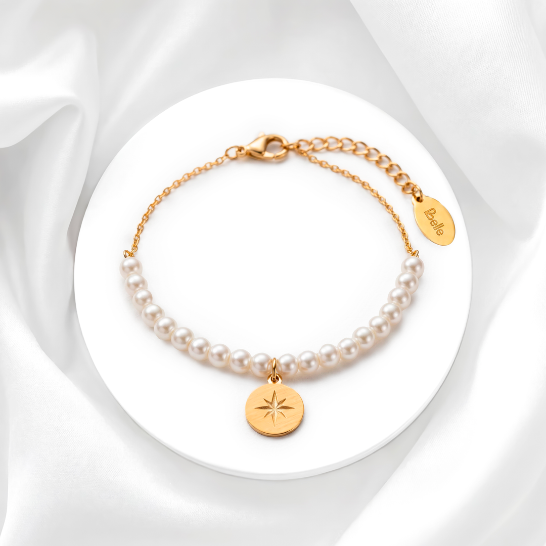 Pulsera para mujer marca Belle compuesta por perlas blancas y eslabones de acero bañado en oro de 18k con un dije colgante de medalla circular con grabado de estrella.