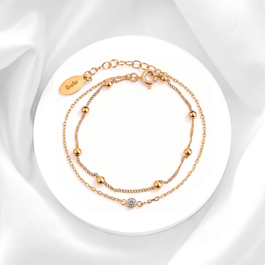 Pulsera doble cadena de mujer en acero quirúrgico 316 baño oro 18k con un cristal blanco solitario y balines dorados lisos pulidos sobre base circular.