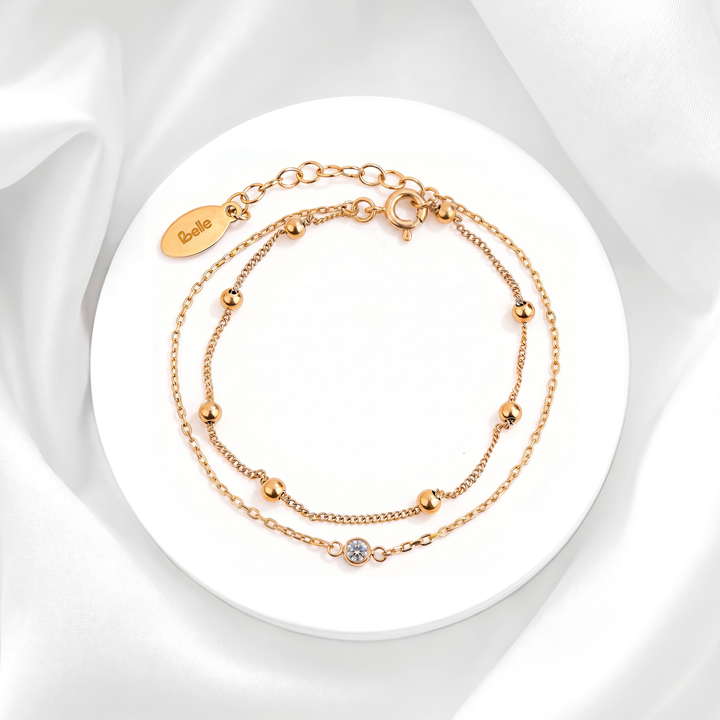 Pulsera doble cadena de mujer en acero quirúrgico 316 baño oro 18k con un cristal blanco solitario y balines dorados lisos pulidos sobre base circular.