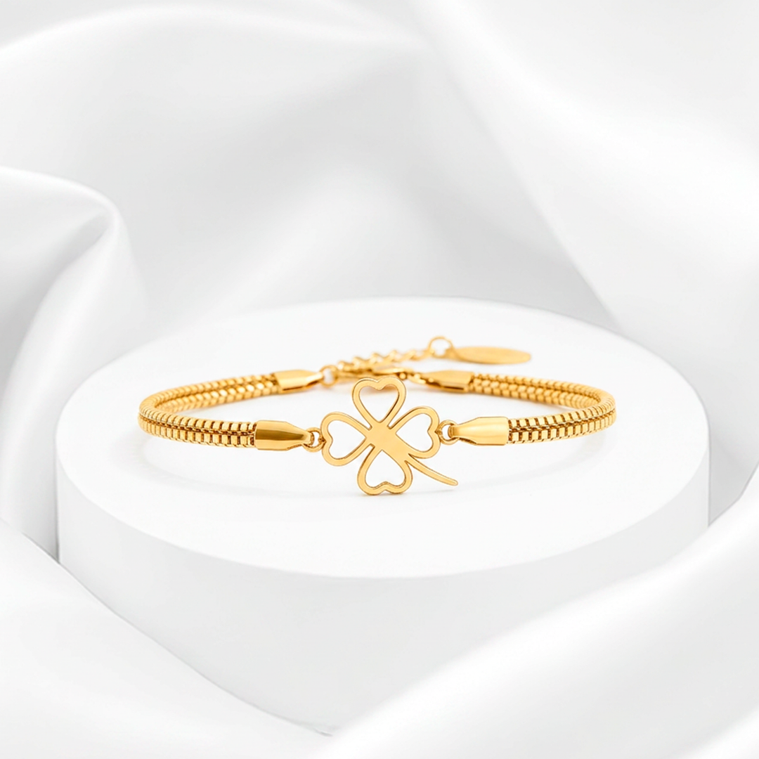 Pulsera de mujer con baño de oro de 18 quilates en acero quirúrgico 316, con doble cadena de eslabones cúbicos y un dije central de trébol calado con corazones huecos.