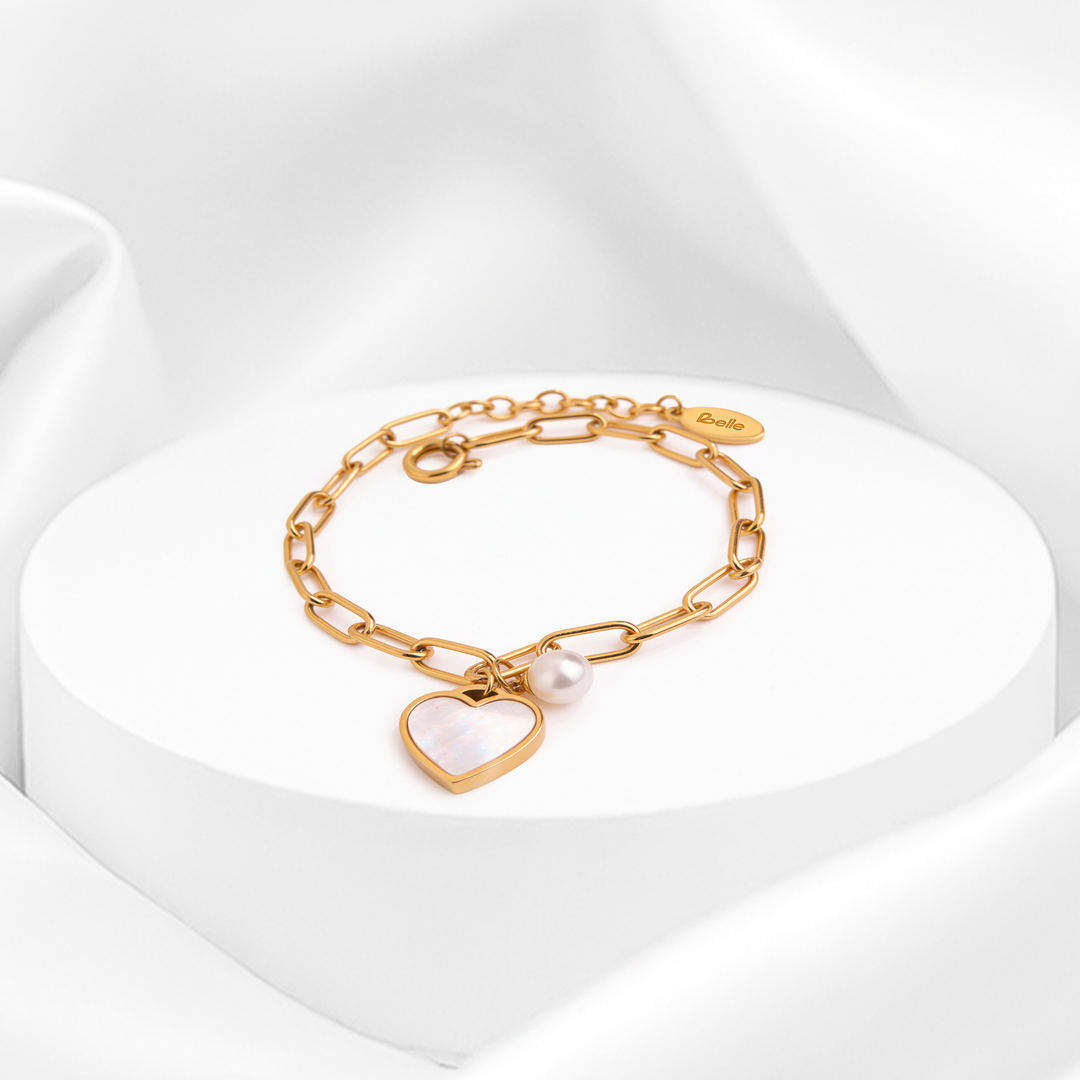 Pulsera dorada de eslabones para mujer en acero quirúrgico 316 baño oro 18 quilates con dije de corazón nacarado blanco y detalle de perla sobre soporte circular.