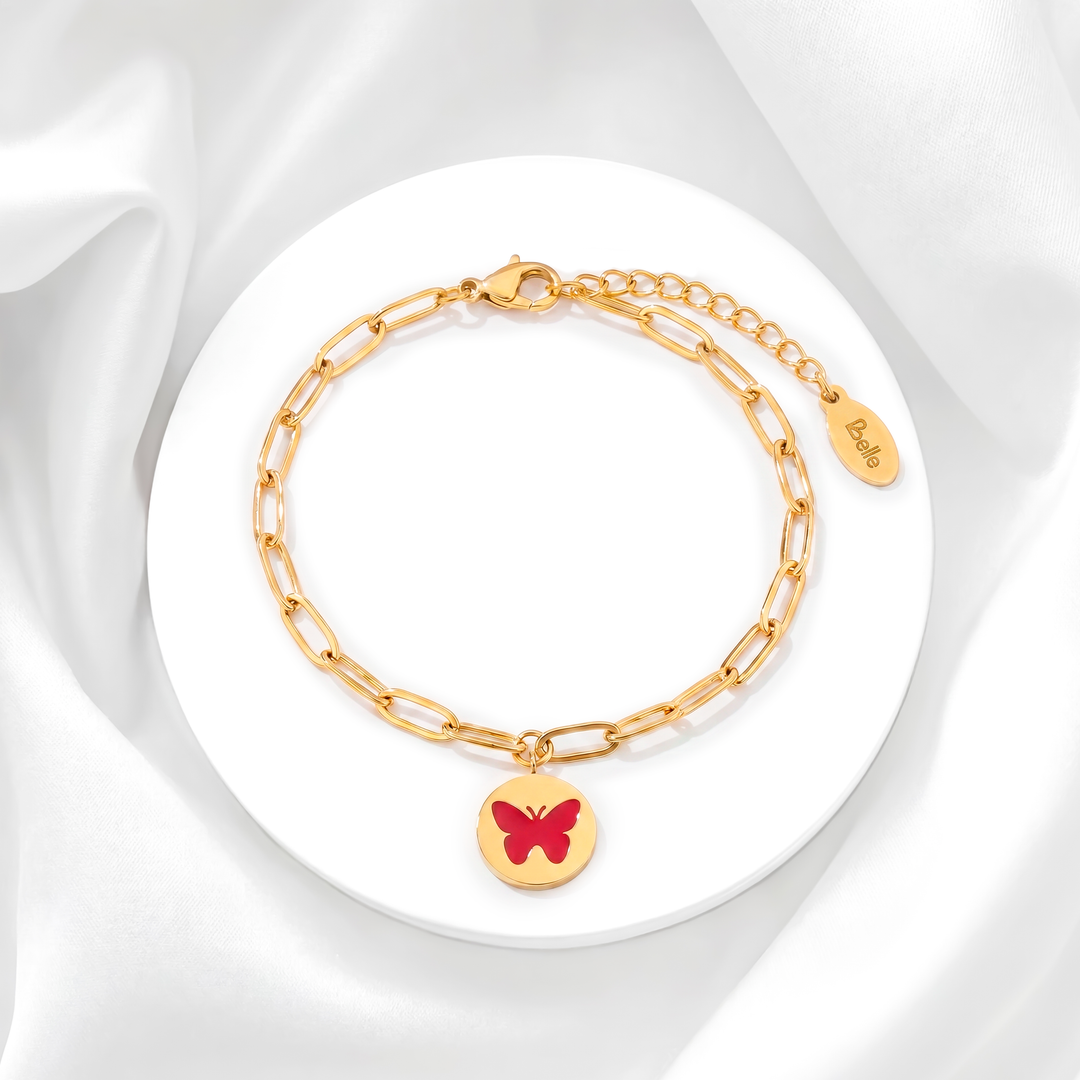 Pulsera para mujer marca Belle con cadena fina de eslabones de acero bañado en oro de 18k y dije de medalla circular con una mariposa esmaltada en color rojo.