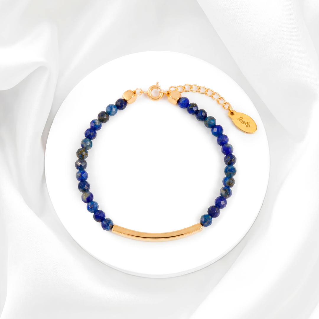 Pulsera para mujer marca Belle fabricada en acero bañado en oro de 18k con una hilera de moisanitas color azul zafiro y una placa rectangular central lisa y pulida.