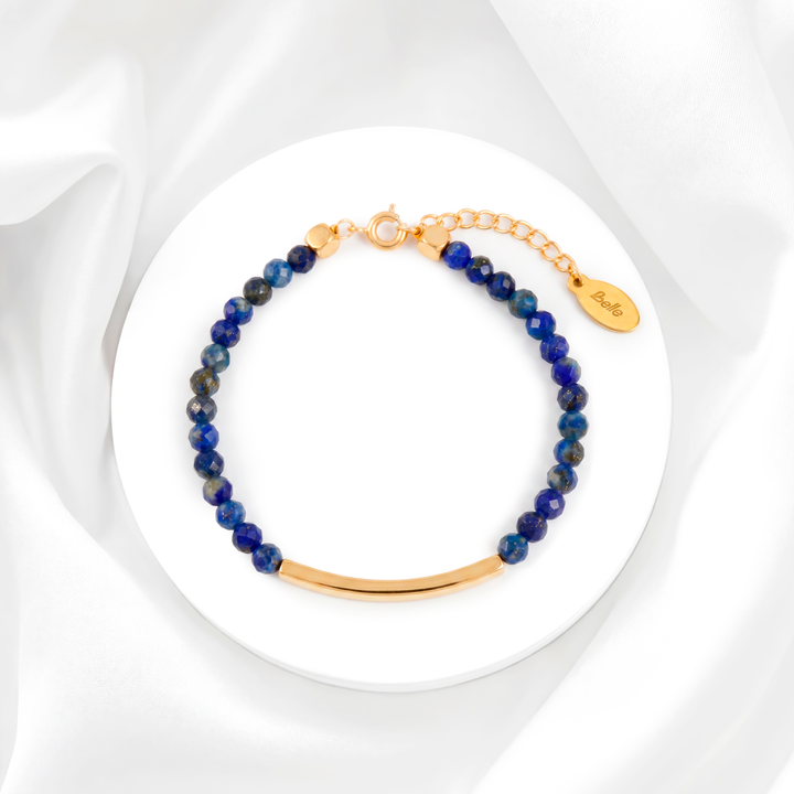 Pulsera para mujer marca Belle fabricada en acero bañado en oro de 18k con una hilera de moisanitas color azul zafiro y una placa rectangular central lisa y pulida.