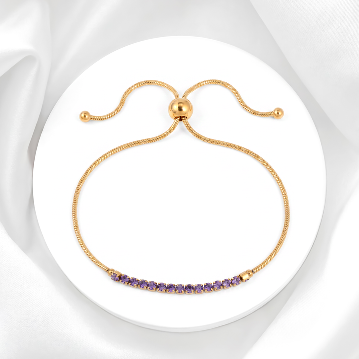 Pulsera ajustable para mujer marca Belle estilo tennis en acero bañado en oro de 18k con carril de cristales strass blancos y tres cristales centrales color lila.