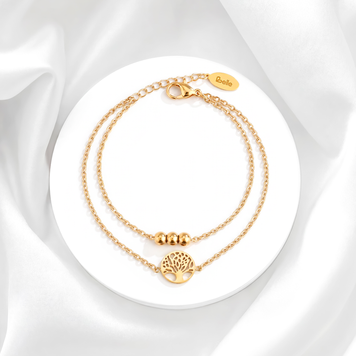 Pulsera de mujer con doble cadena en acero quirúrgico 316 con baño de oro de 18k, detallada con tres esferas doradas y un dije circular calado del Árbol de la Vida.