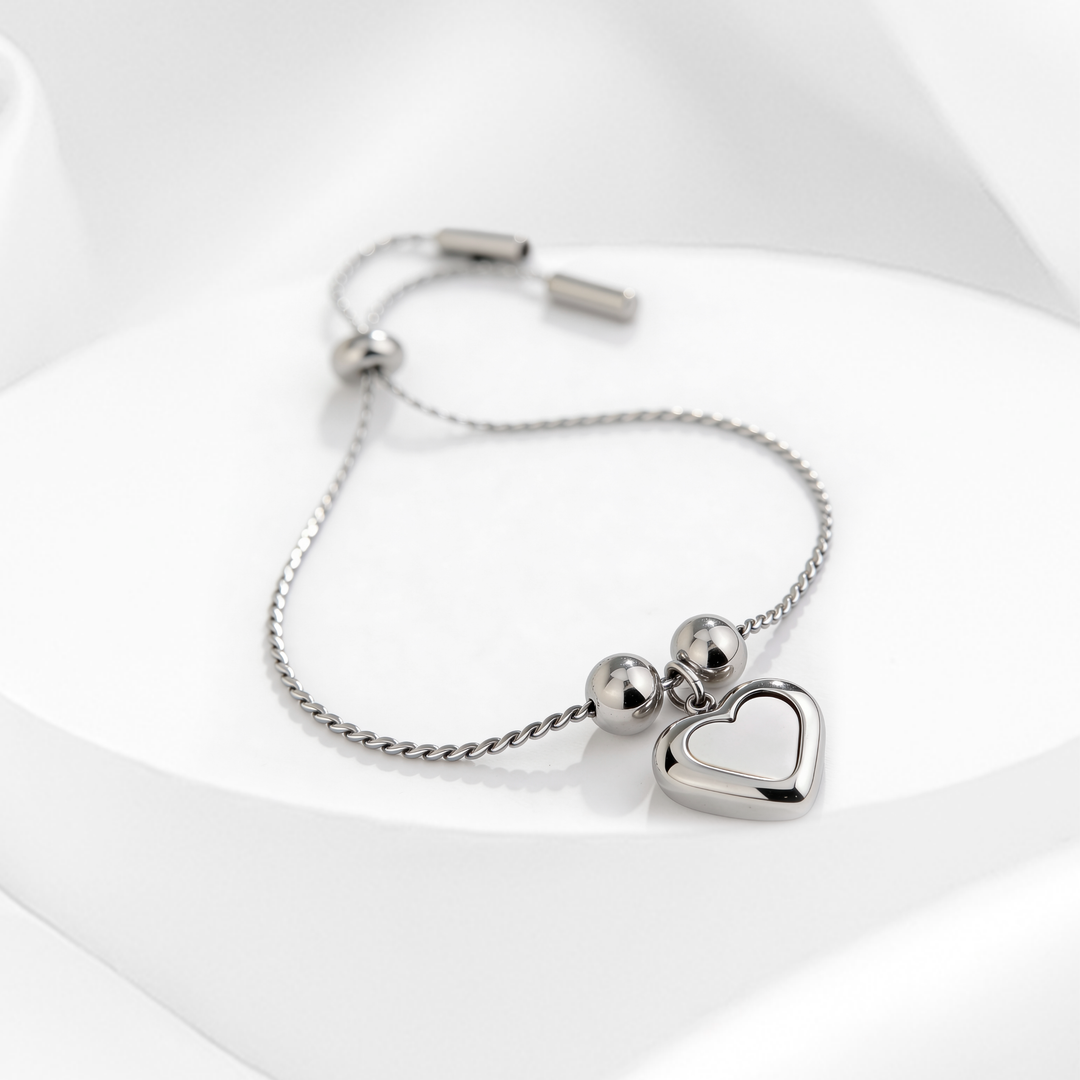 Pulsera plateada de mujer en acero 316L ajustable con dije de corazón nacarado sobre fondo blanco.