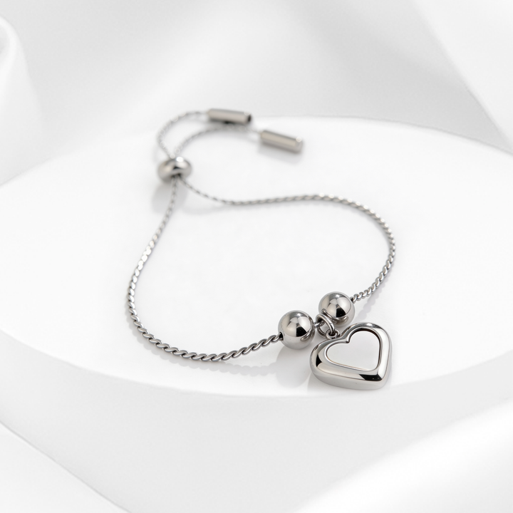 Pulsera plateada de mujer en acero 316L ajustable con dije de corazón nacarado sobre fondo blanco.