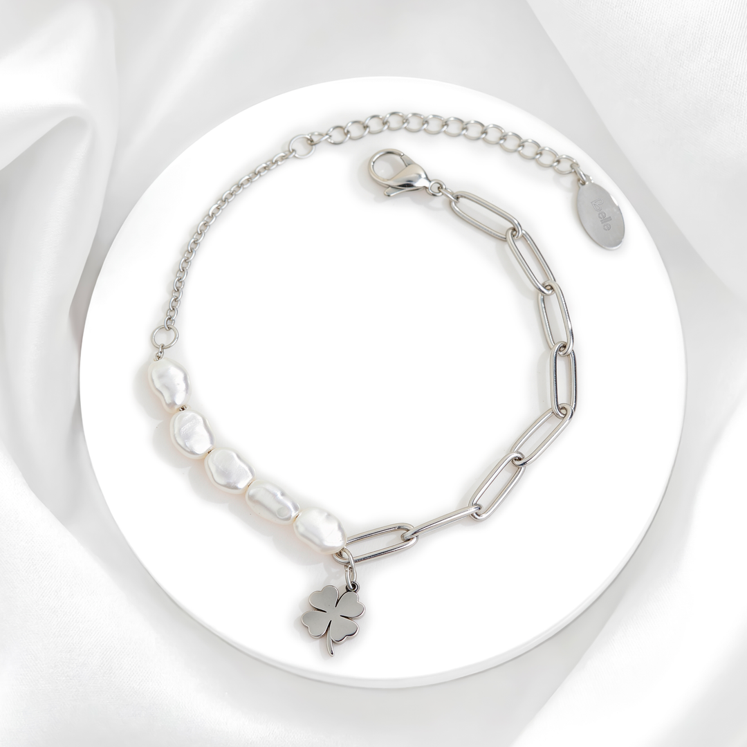 Pulsera plateada de mujer en acero 316L con perlas de río naturales, cadena de eslabones paperclip y dije de trébol sobre soporte circular blanco.