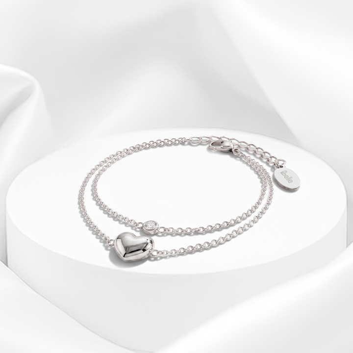 Pulsera plateada de doble cadena fina para mujer en acero quirúrgico 316 con un dije de corazón abombado pulido y un cristal blanco solitario sobre superficie redonda.