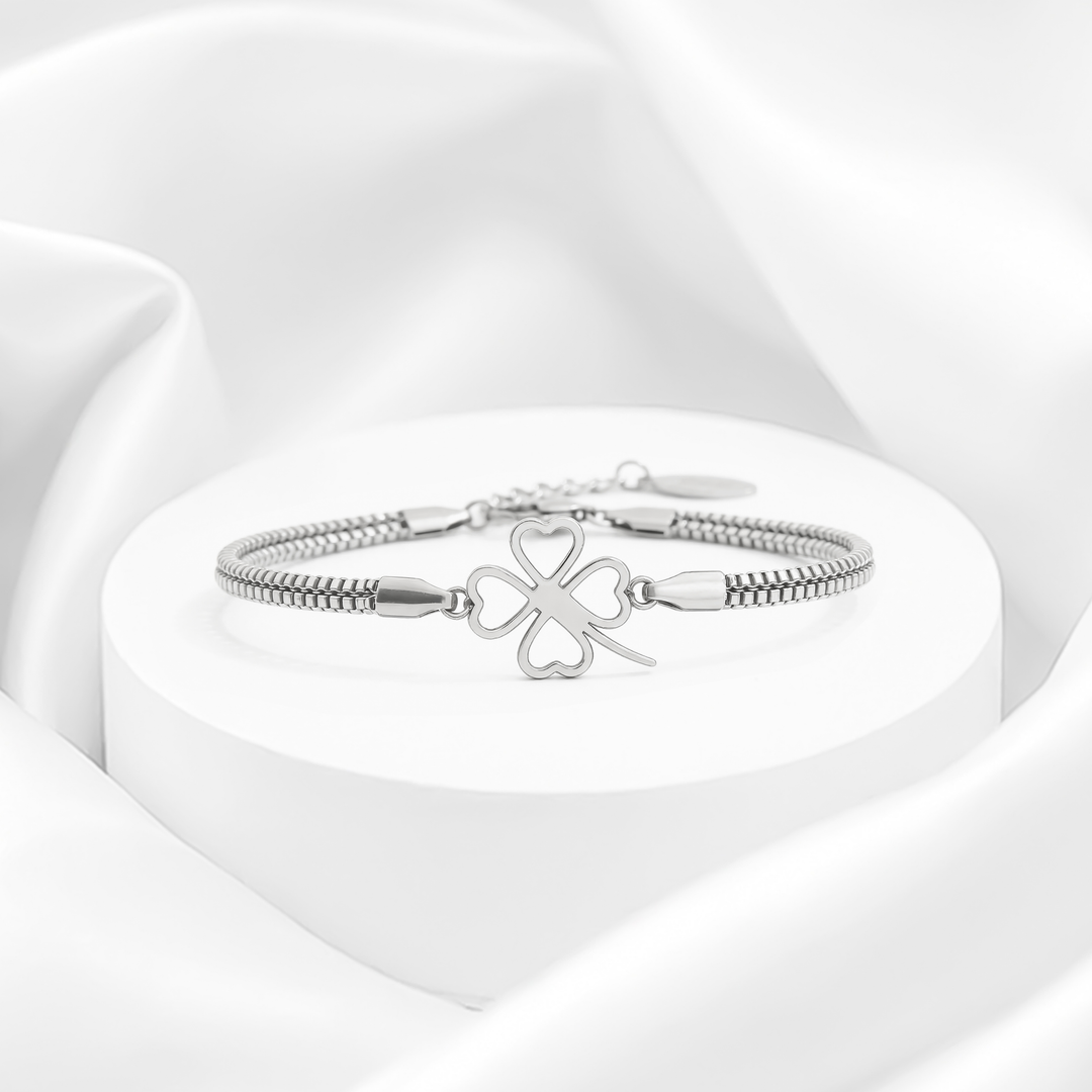 Pulsera plateada de mujer con doble cadena de eslabones cuadrados estilo veneciano en acero quirúrgico 316, con dije central de trébol de cuatro hojas calado con corazones huecos.