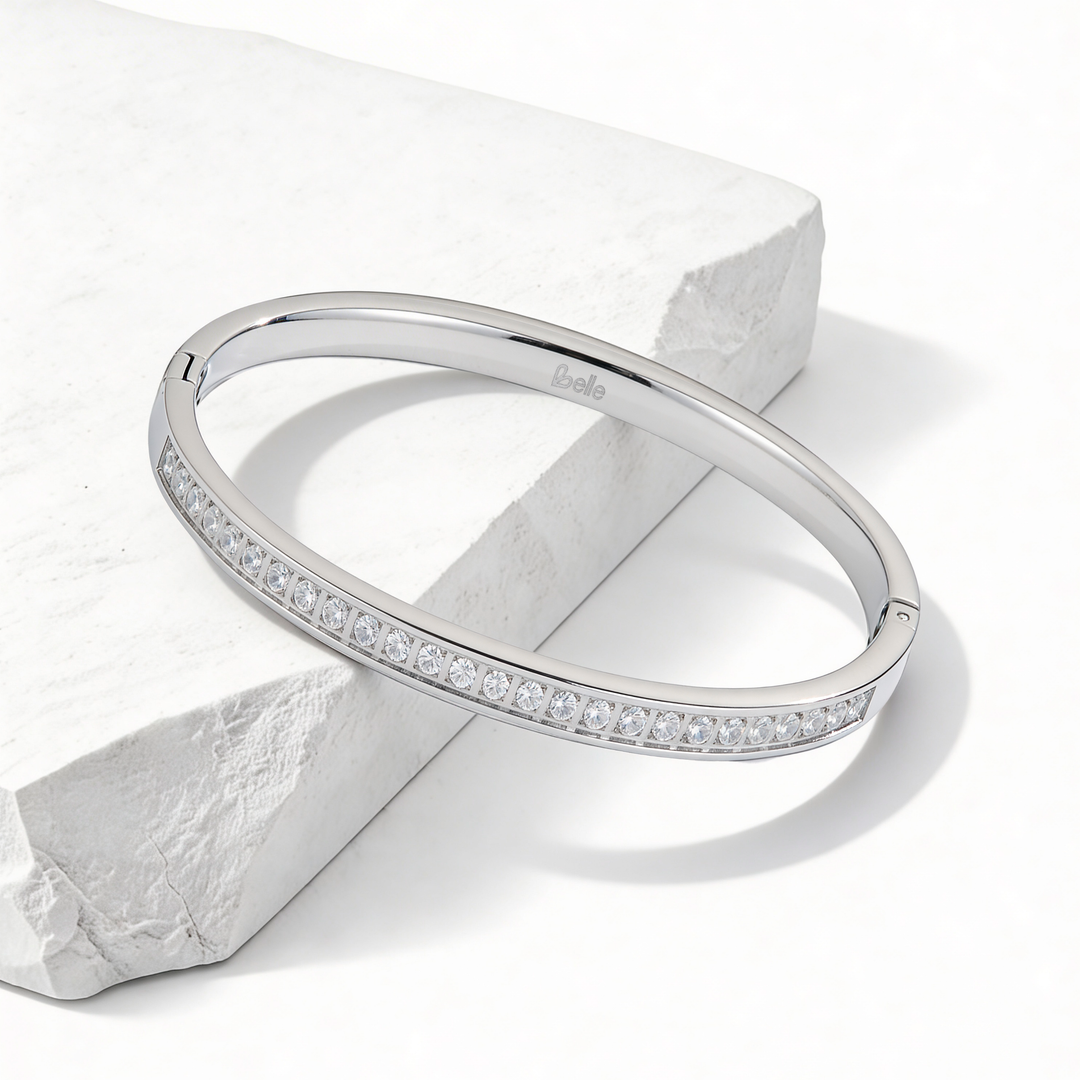 Brazalete rígido de mujer en acero quirúrgico 316 plateado con medio contorno frontal cubierto de cristales blancos brillantes engastados en pavé sobre base redonda.