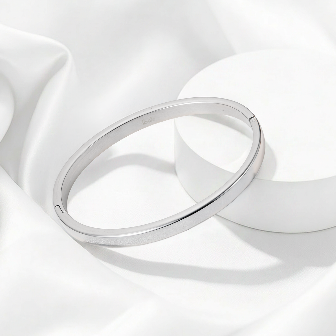 Brazalete rígido de perfil plano para mujer en acero quirúrgico 316 plateado, con superficie totalmente lisa pulida a espejo y contorno ovalado.