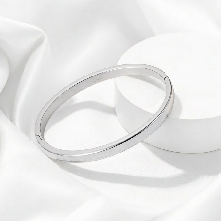 Brazalete rígido de perfil plano para mujer en acero quirúrgico 316 plateado, con superficie totalmente lisa pulida a espejo y contorno ovalado.
